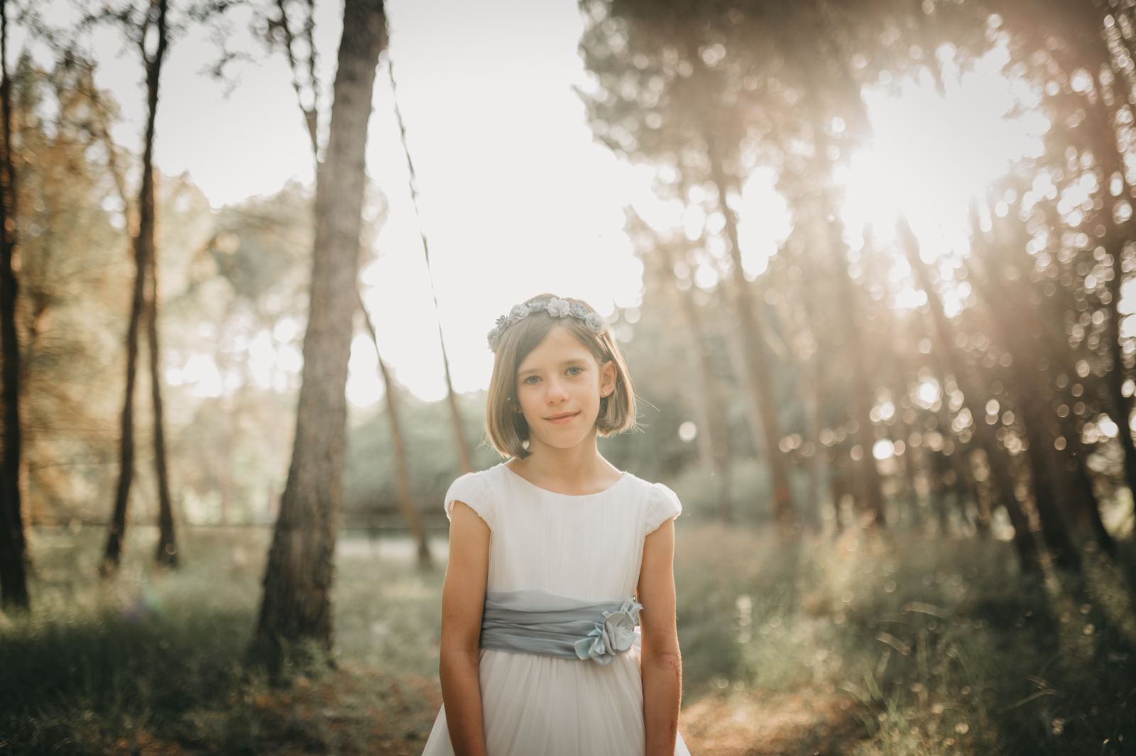 Niña con su vestido de comunión en un pinar a contraluz