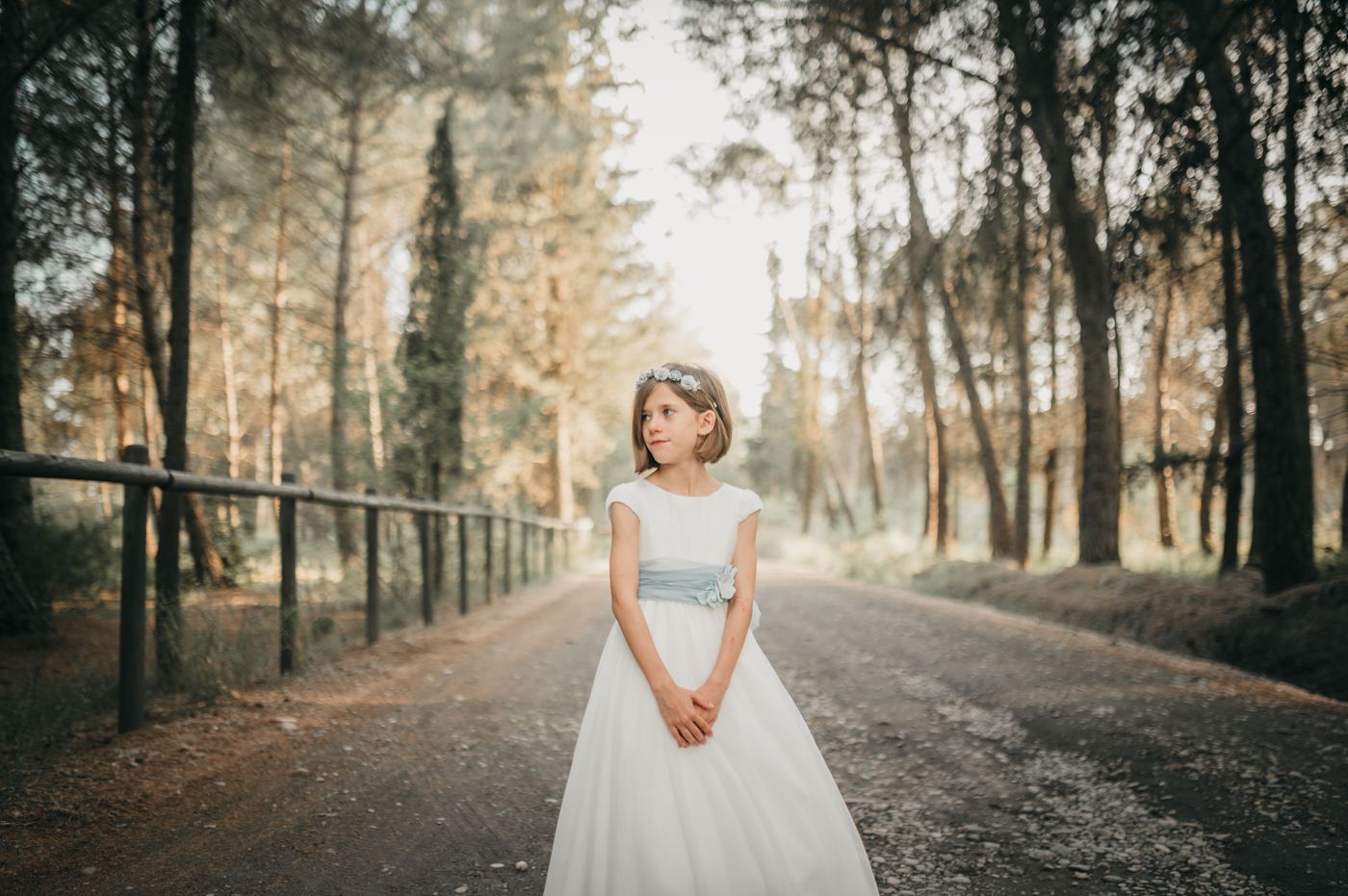 Niña de comunión en un camino entre árboles