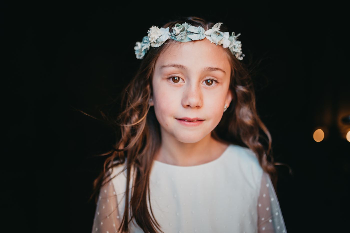 Retrato de niña de comunión con corona de flores sobre fondo oscuro