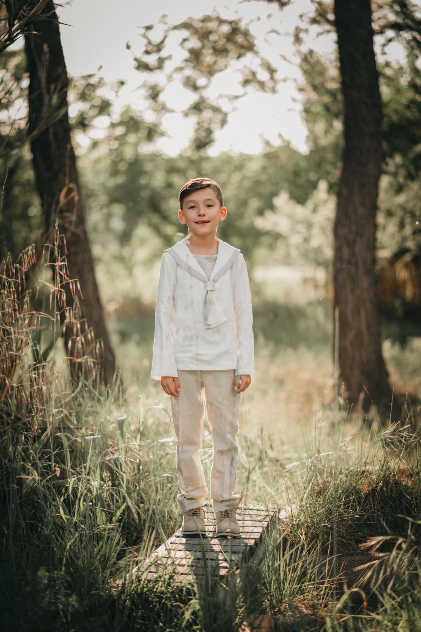 Niño con traje de comunión entre los pinos