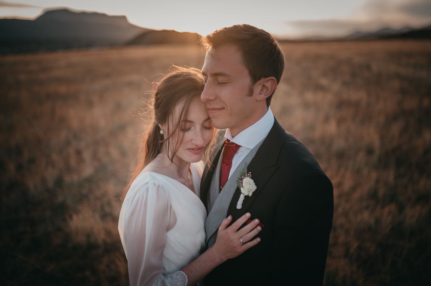 Novios abrazados con luz dorada en el campo