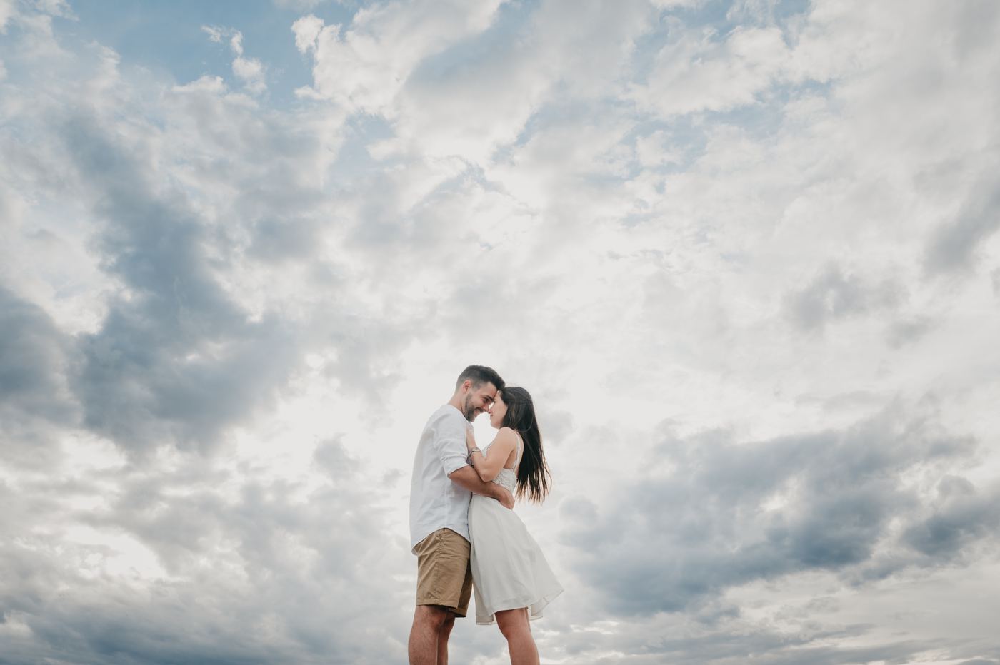Pareja abrazada bajo un cielo de nubes en su preboda